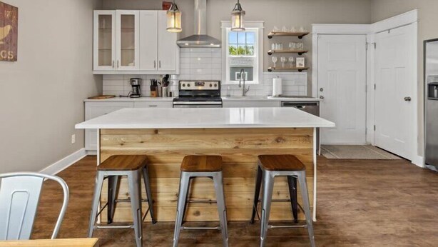 Una cocina moderna con una isla central, taburetes de bar, armarios blancos e iluminación colgante.