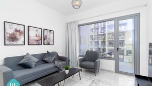 Een moderne woonkamer met een grijze bank, een grijze fauteuil, een zwarte salontafel en een groot raam met uitzicht op gebouwen.