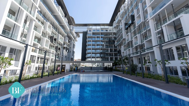Een modern appartementencomplex met een centraal gelegen zwembad, balkons en een heldere lucht.