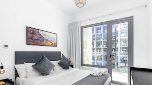 Een moderne hotelkamer met een groot bed, een grijs hoofdeinde en uitzicht op de stad door een glazen schuifdeur.