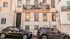 A building with a cobblestone street, two parked cars, and a sign that reads "RUA DO CONDE."