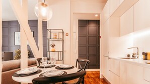 A modern kitchen with white cabinets, a dining area with a round table set for four, and a wooden floor.