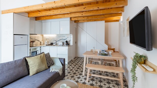 A compact living space with a kitchenette, a sofa, a dining table, and a TV mounted on the wall. - Pestana Houses (Porto)