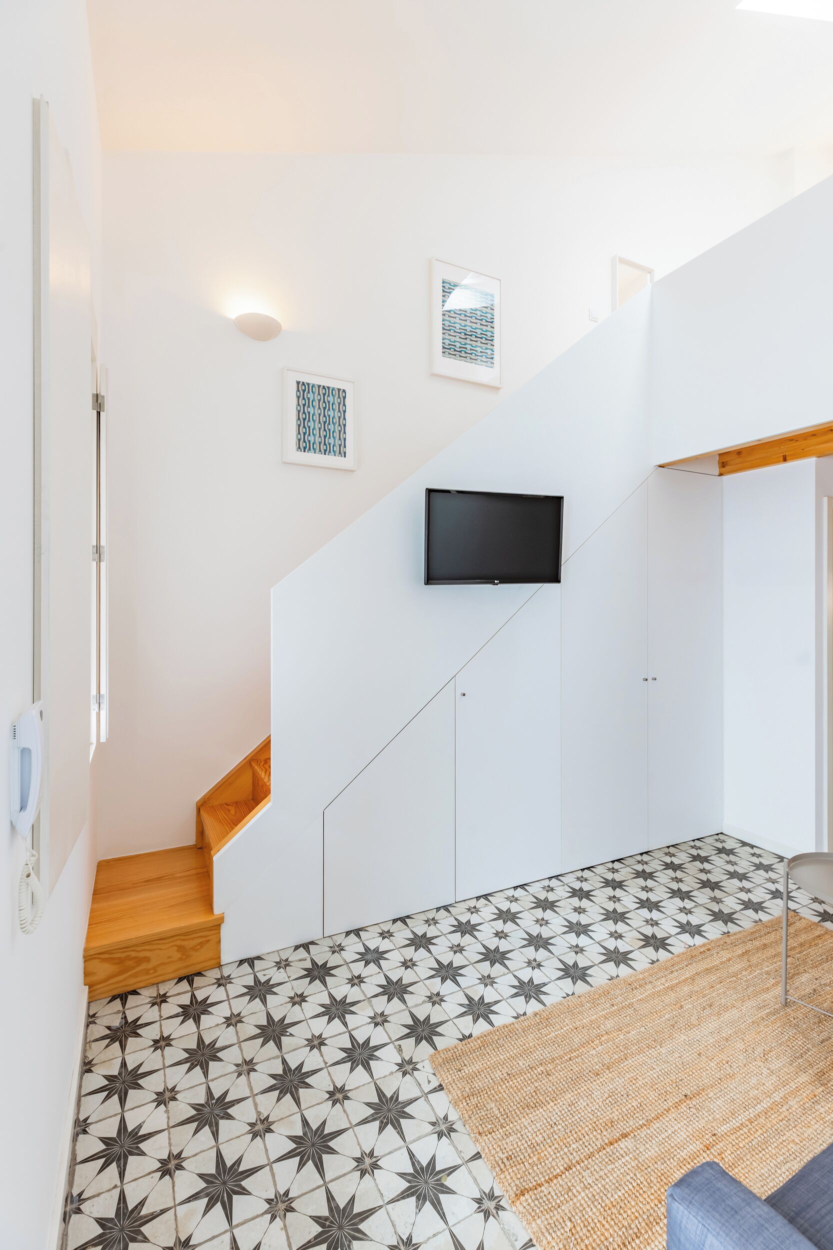 Eine Treppe mit einem gemusterten Boden, ein wandmontierter Flachbildfernseher und eine Holztür.