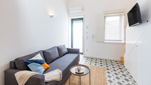 A modern living room with a grey sofa, a small round table with a cup, a TV mounted on the wall, and a patterned floor. - Pestana Houses (Porto)