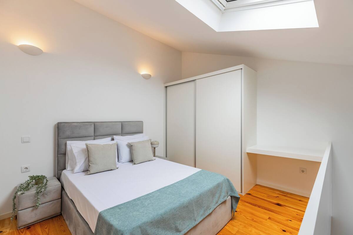 A bedroom with a bed, bedside tables, a wardrobe, and a skylight.