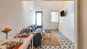 A modern living room with a sofa, dining table set for two, and a TV mounted on the wall. - Pestana Houses (Porto)