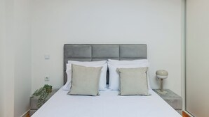 A neatly made bed with white bedding and two pillows, a grey headboard, and a bedside table with a lamp. - Pestana Houses (Porto)