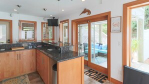 Cocina moderna con encimeras de granito, armarios de madera y una isla grande. Hay una puerta corrediza de vidrio que da a un patio con mobiliario exterior.