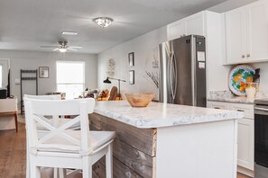 Een moderne keuken met witte kasten, een marmeren aanrechtblad, een groot eiland en een roestvrijstalen koelkast.