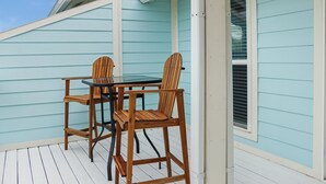 Un espace extérieur abrité, aménagé avec deux chaises en bois et une table, situé à côté d’une fenêtre équipée de stores.