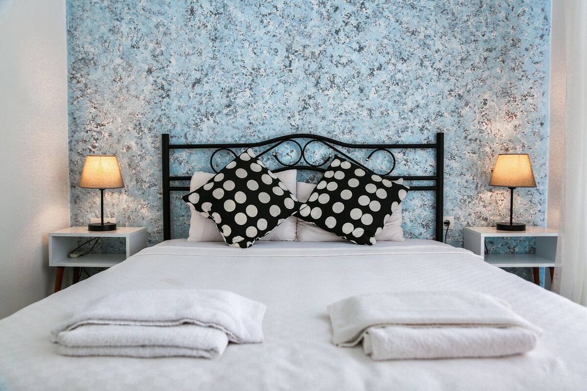 Un lit bien fait, avec du linge de lit blanc, deux coussins à pois noirs et blancs, et deux lampes de chevet posées sur des tables de chevet assorties.