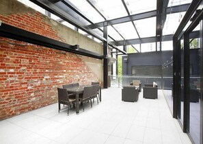 A modern outdoor patio with a brick wall, glass enclosure, and outdoor seating.
