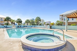 A swimming pool with a hot tub, lounge chairs, and palm trees.