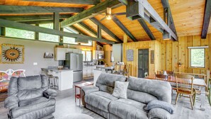 Ein geräumiger Wohnbereich mit grauem Sofa, einem Holzesstisch und einer Küche im Hintergrund.