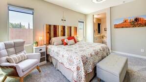 Un dormitorio con una cama grande, una silla, un banco, una mesita de noche y una lámpara de pared.
