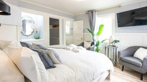 A bedroom with a large bed, a bedside table, a chair, a TV mounted on the wall, and a wardrobe. - Capitola Village Bungalow - 2 Blocks from the Sand (Capitola)