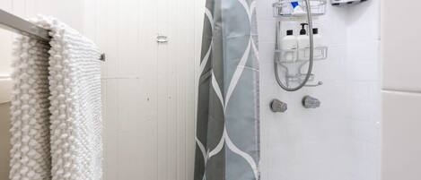 Une salle de bain équipée d’une douche, d’un porte-serviettes et d’un distributeur de savon fixé au mur.