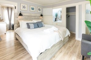A bedroom with a wooden bed, white bedding, a bedside table, a mirror, and a window with curtains.