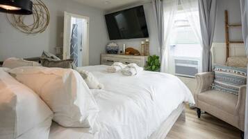 A bedroom with a large bed, a TV mounted on the wall, a bedside table with a lamp, and a window with curtains.