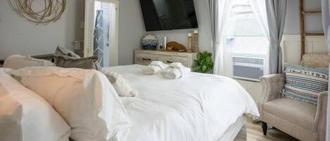 Un dormitorio con cama, televisor, cómoda y ventana con cortinas.
