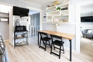 Una cocina compacta con una mesa de madera y sillas negras, un microondas y un tostador sobre una estantería.