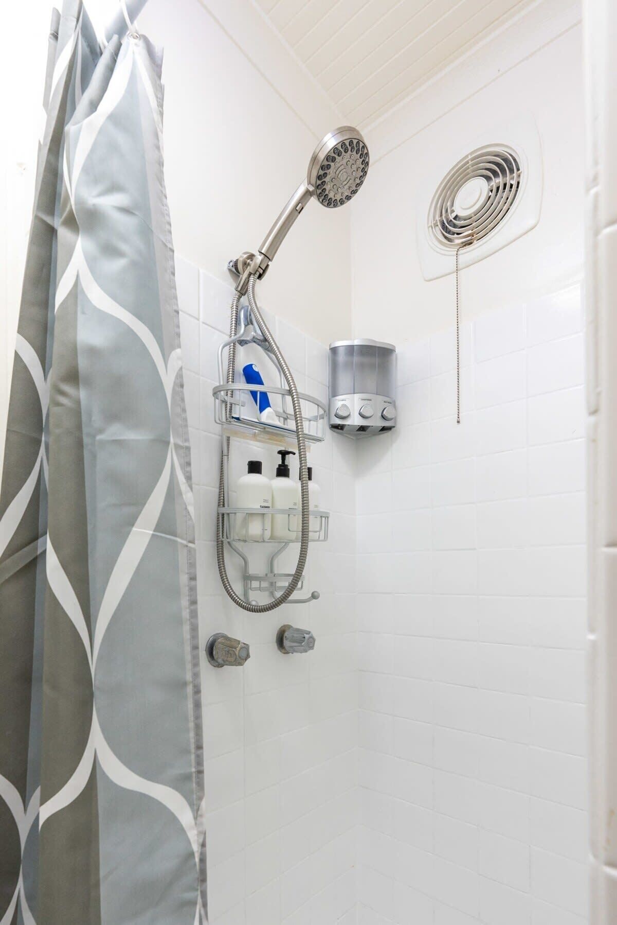 Un baño con ducha, secamanos y dispensador de jabón.