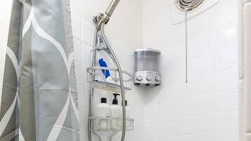 Un baño con ducha, secamanos y dispensador de jabón.