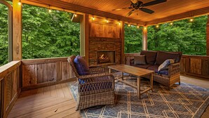 A wooden deck with wicker furniture, a fireplace, and string lights.