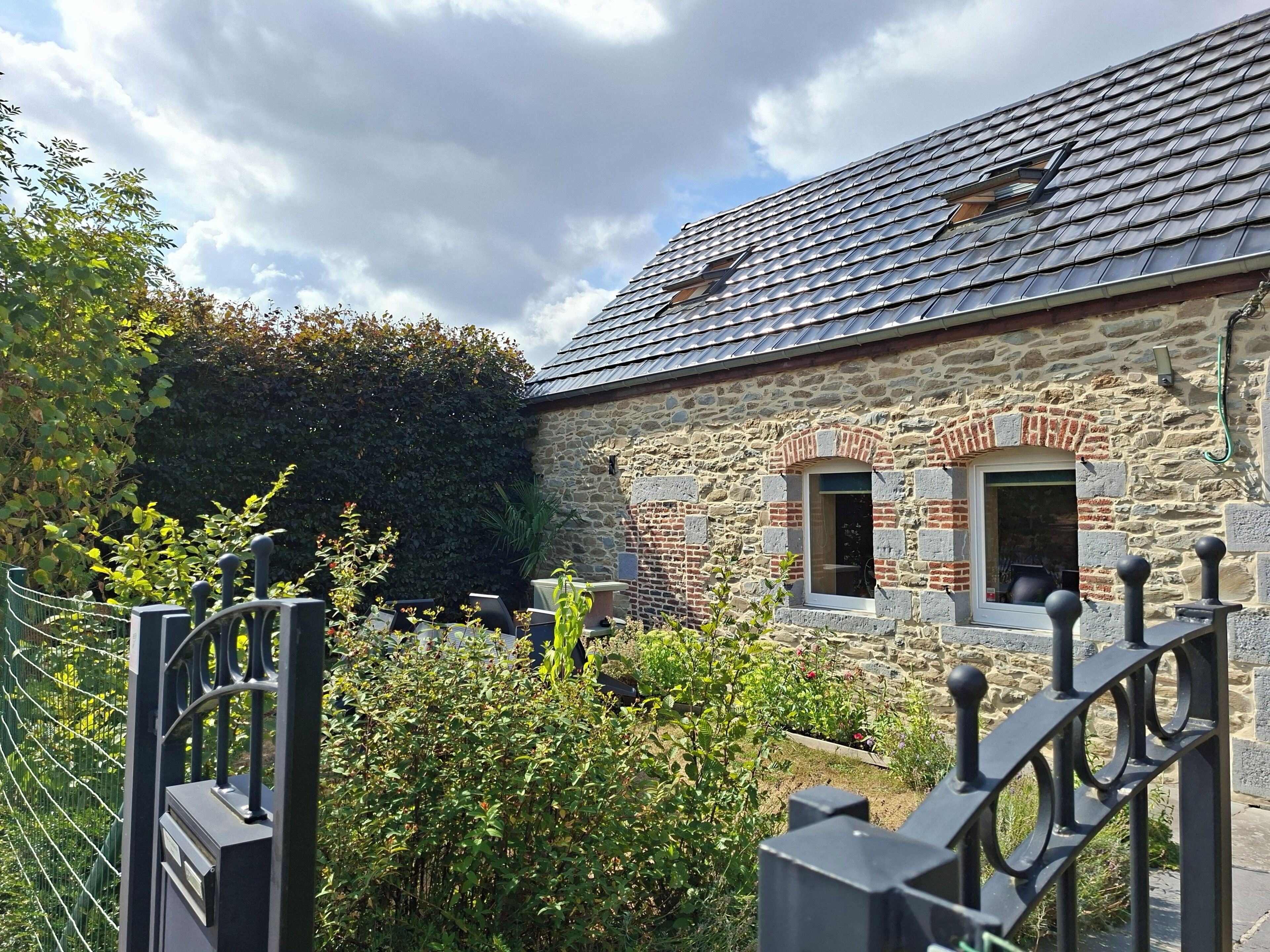 Un bâtiment en pierre avec un toit recouvert de tuiles, une petite fenêtre et un portail.