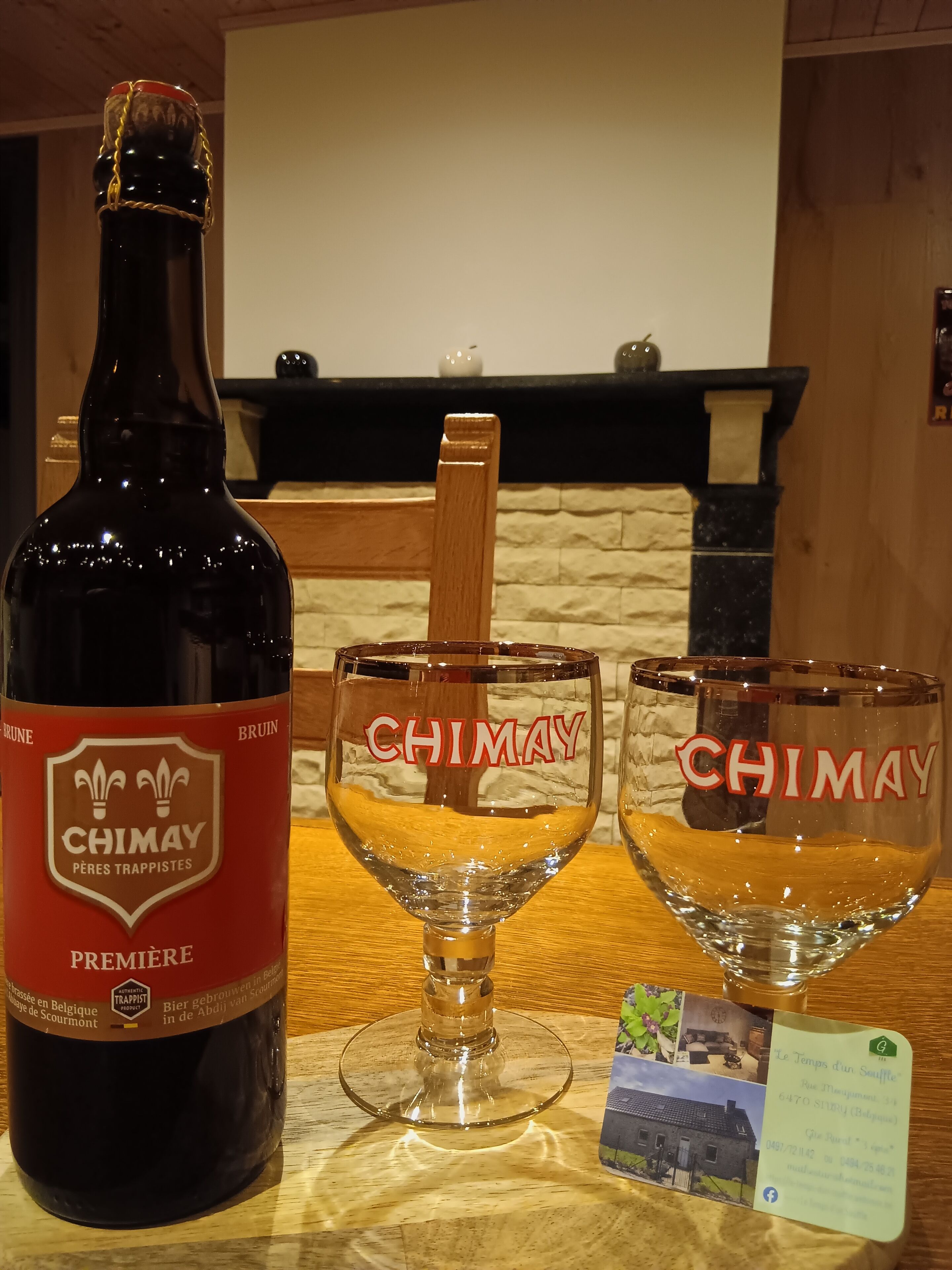 Una bottiglia di birra Chimay, due bicchieri di Chimay e un biglietto da visita su un tavolo di legno.