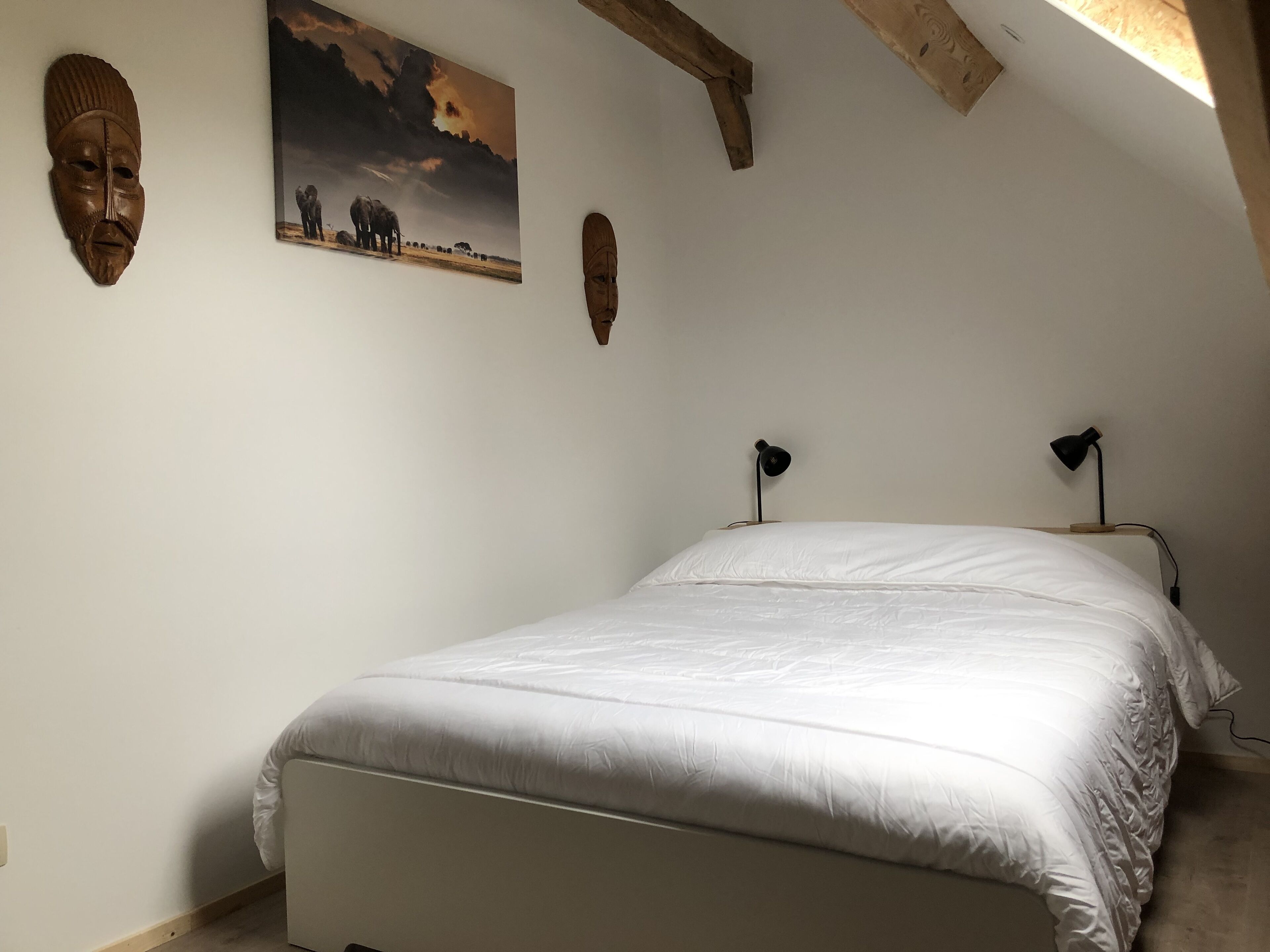 Een slaapkamer met een bed, twee wandlampen en een schilderij van olifanten.