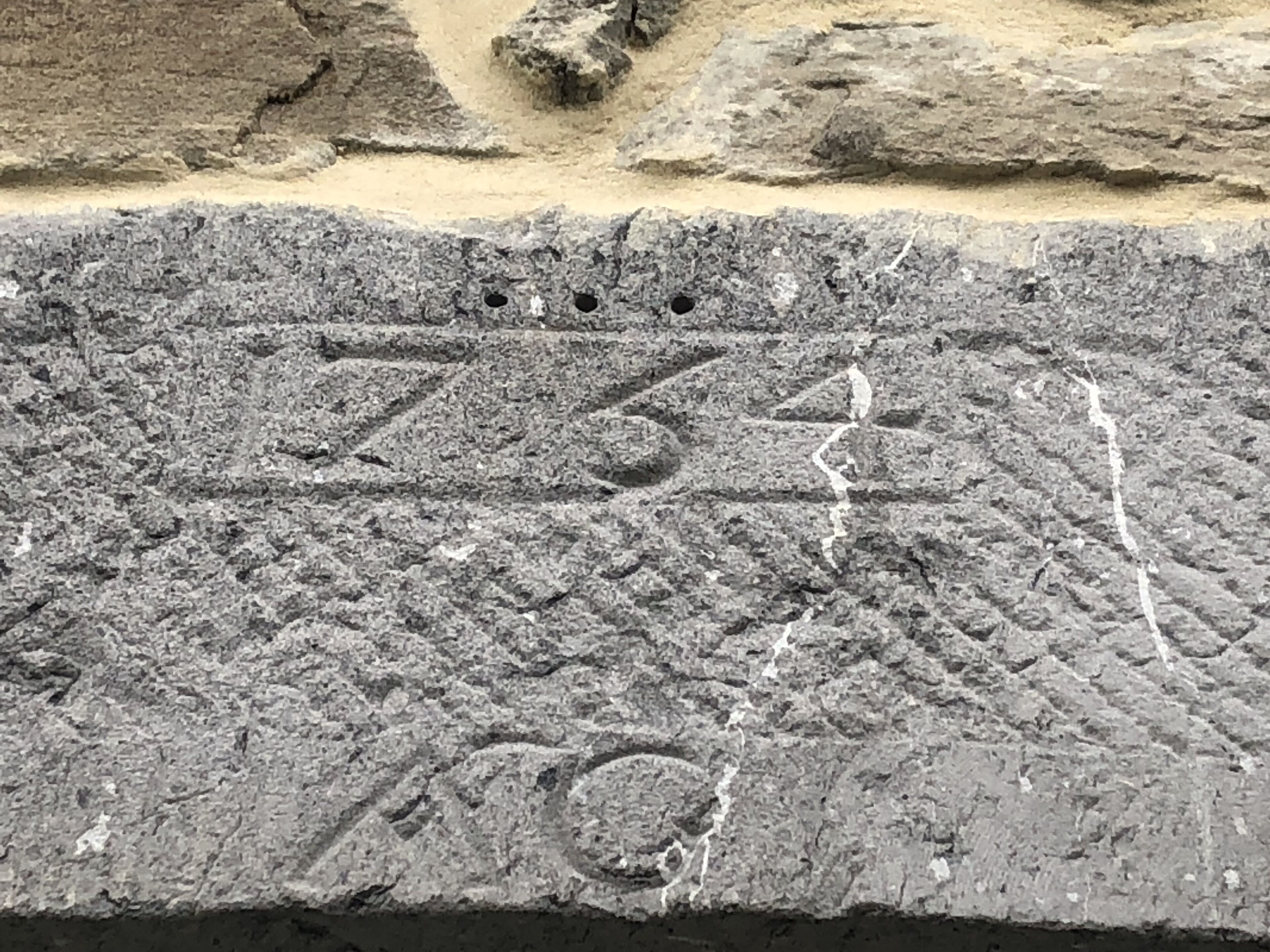 A stone surface with engraved numbers and symbols, possibly a monument or historical marker.