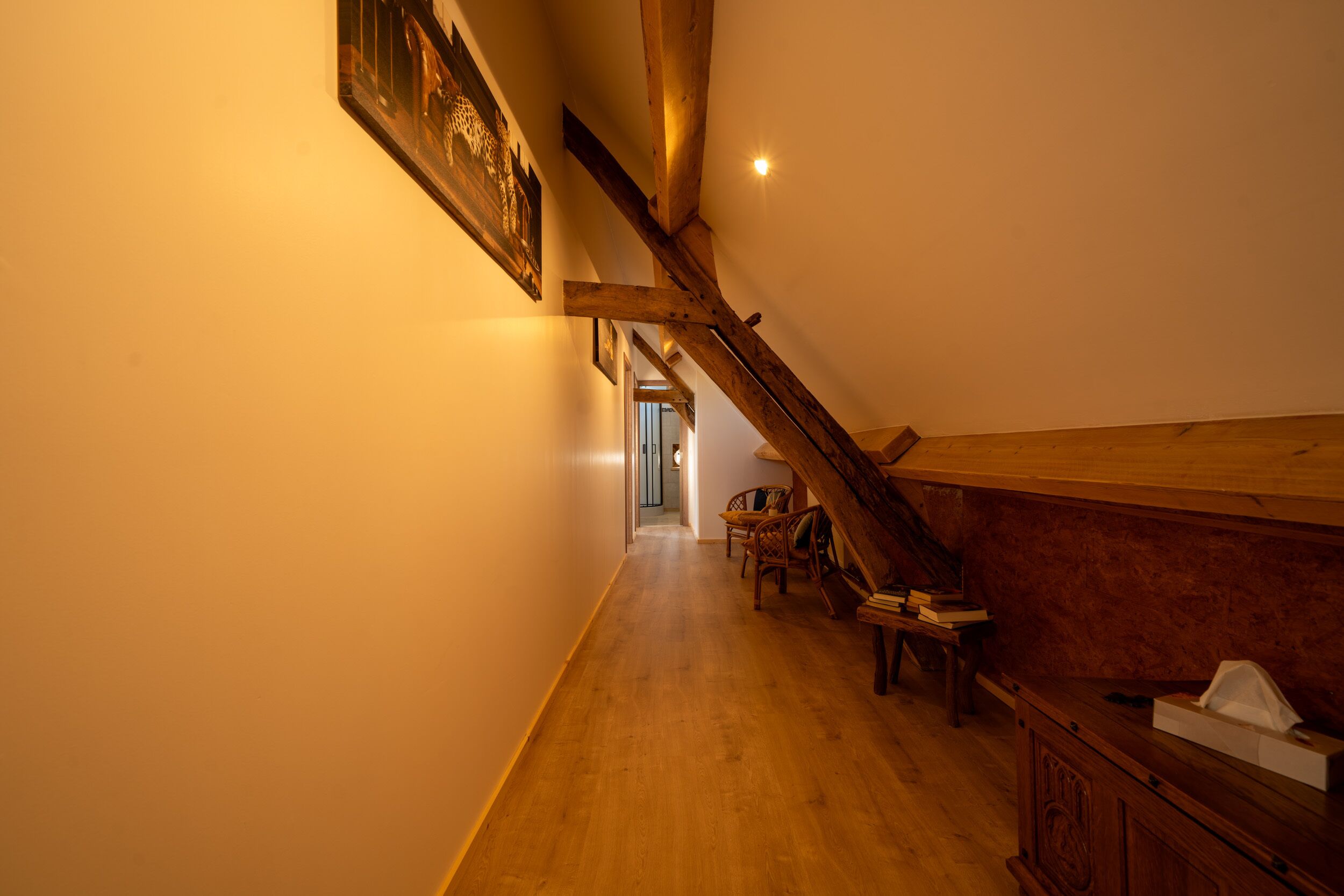 Een houten trap die naar een hoger verdiep leidt, een houten bank met boeken, en een ingelijst beeld aan de muur.