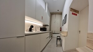 A compact kitchen with a microwave, kettle, and sink. There is a small stool and a fire extinguisher mounted on the wall. - Neo Porto Family & Friends local accommodation. (União de Freguesias do Centro)