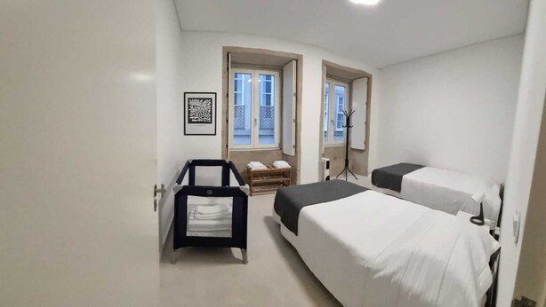 A small, clean room with two beds, a desk, and a chair. There are windows and a door. - Neo Porto Family & Friends local accommodation. (União de Freguesias do Centro)