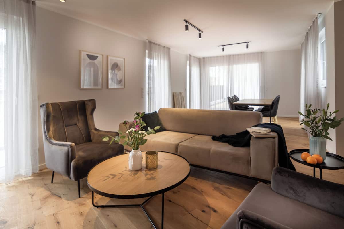 Ett modernt vardagsrum med en soffa, fåtölj, soffbord och en matplats med bord och stolar.