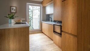 A modern kitchen with wooden cabinetry, a white countertop, and a built-in oven. - Sleep Inn Medienhafen Suites (Düsseldorf)