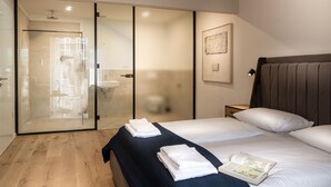 A modern bedroom with a large bed, a glass shower enclosure, and a bedside table with a lamp. - Sleep Inn Medienhafen Suites (Düsseldorf)