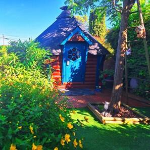 A small wooden cabin with a blue door, surrounded by greenery and a brick pathway. - La Cabane de mes Rêves (Rousson)