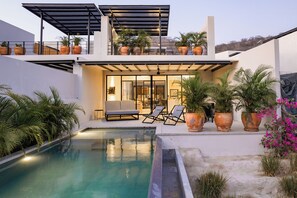 A modern house with a swimming pool, outdoor seating, and potted plants.