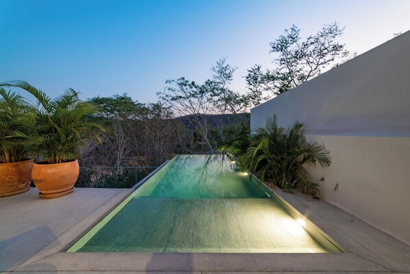 A rectangular swimming pool with a textured surface, surrounded by a low wall and potted plants.