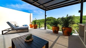 A balcony with a lounge chair, a table with a cactus, and large potted plants. - Modern Villa Overlooking Lush National Park (Huatulco)