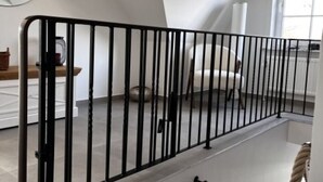 Una habitación con barandilla de metal negro, una barrera de cuerda y una pared blanca.