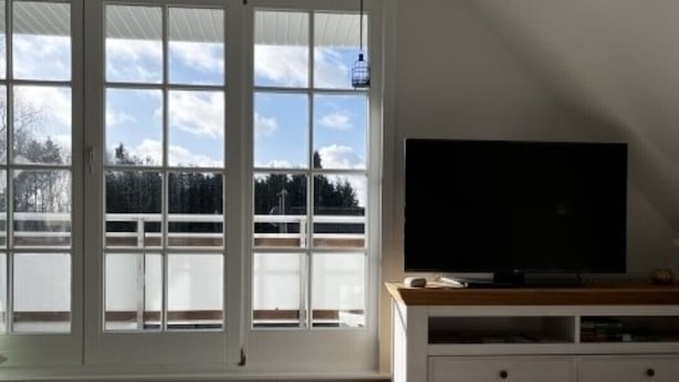 Una habitación con un ventanal grande, un televisor de pantalla plana sobre un soporte de madera y una silla blanca.