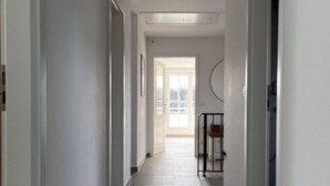 Un estrecho pasillo con paredes blancas y piso de baldosas, que conduce a una puerta al final.
