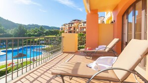 A balcony with lounge chairs, a swimming pool, and a view of a hillside. - Premium apartment in Benahavis with balcony (BENAHAVIS)