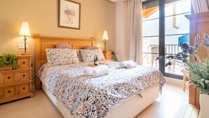 A neatly arranged bedroom with a large bed, two bedside tables with lamps, a framed artwork on the wall, and a balcony with plants. - Premium apartment in Benahavis with balcony (BENAHAVIS)