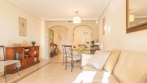 A spacious living room with a beige sofa, a wooden bookshelf, and a dining area with a table and chairs. - Premium apartment in Benahavis with balcony (BENAHAVIS)