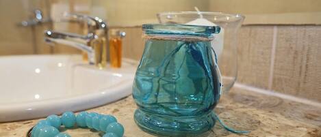 Un baño con un lavamanos, un tarro de vidrio y una pulsera azul de cuentas sobre la encimera.